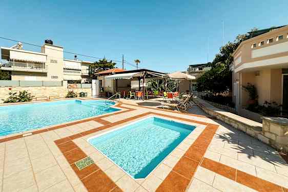 Kaksi ulkouima-allasta, ympäröity aurinkotuoleilla ja varjoalue värikkäillä tuoleilla. (Tekoälyn luoma teksti)