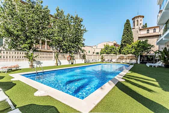 Ulkouima-allas, jonka ympärillä on aurinkotuoleja, ympäröivä kyläarkkitehtuuri ja vehreys. (Tekoälyn luoma teksti)