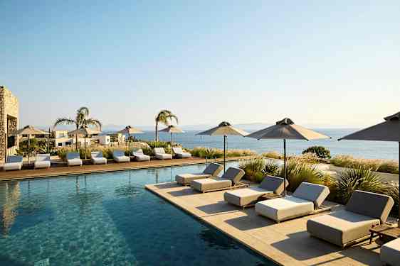 Uima-allasalue aurinkotuoleineen ja varjoineen, näkymä merelle. (Tekoälyn luoma teksti)