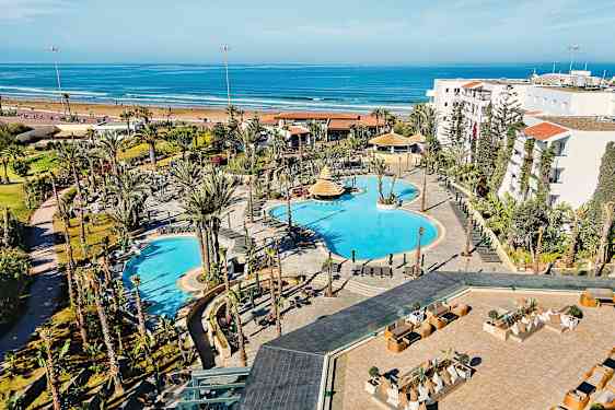 Hotellialue, jossa uima-altaita ja ympäröivää puutarhaa, sijaitsee lähellä hiekkarantaa ja merta. (Tekoälyn luoma teksti)