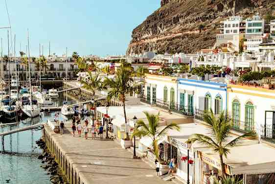 Kuva satamasta purjeveneineen, joita ympäröivät värikkäät rakennukset ja palmupuut. (Tekoälyn luoma teksti)