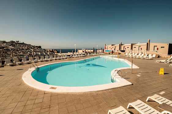 Näkymä ulkouima-altaalle, jota ympäröivät aurinkotuolit ja aurinkovarjot. (Tekoälyn luoma teksti)