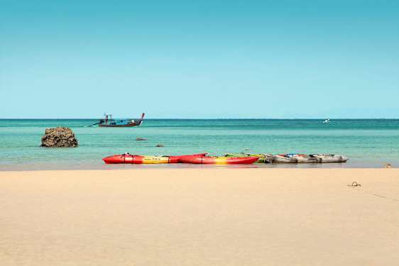 Useita kajakkeja hiekkarannalla, meri ja vene taustalla. (Tekoälyn luoma teksti)