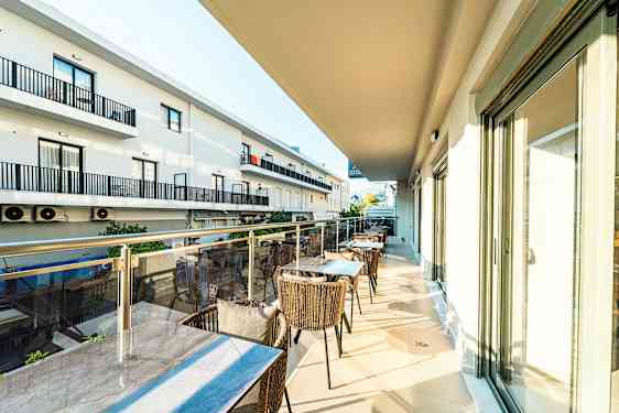 Parveke, jossa pöytiä ja tuoleja, näkymä viereisiin rakennuksiin. (Tekoälyn luoma teksti)