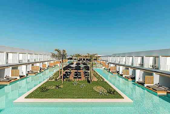 Pitkä uima-allas, jota ympäröivät modernit hotellirakennukset ja aurinkotuolit. (Tekoälyn luoma teksti)