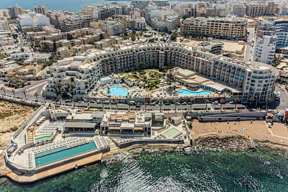 Kuvassa on laaja lomakeskus, jossa on uima-altaita, auringonottoalueita ja ympäröiviä rakennuksia rannikolla. (Tekoälyn luoma teksti)