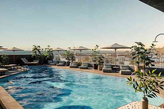 Ulkouima-allas, jossa on aurinkovarjoja, aurinkotuoleja ja kasveja ympärillä. (Tekoälyn luoma teksti)