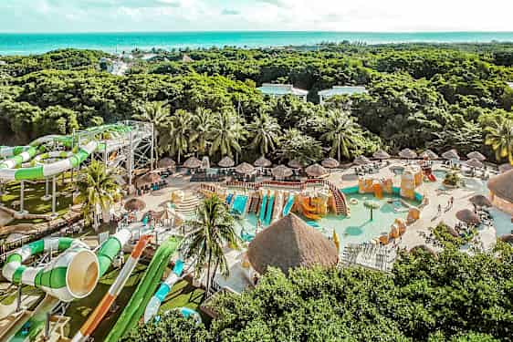 Kuva vesipuistosta, jossa on vesiliukumäkiä, uima-altaita ja vehreyttä taustalla. (Tekoälyn luoma teksti)