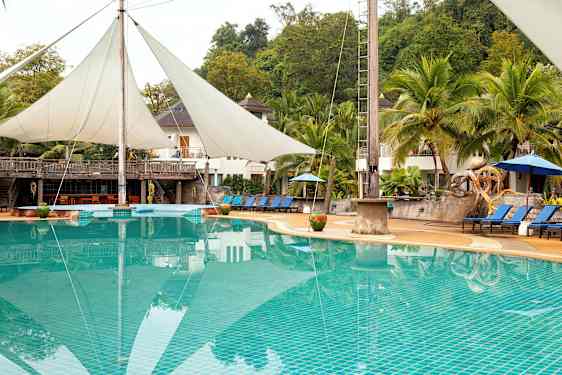 Uima-allas, jossa aurinkotuoleja ja varjoja, ympäröitynä palmupuiden ja rakennusten taustalla. (Tekoälyn luoma teksti)