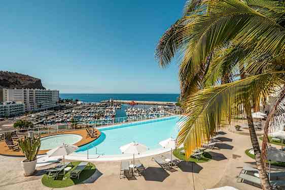 Näköala infinity-altaalle, aurinkotuoleille ja aurinkovarjoille. Taustalla näkyy satama ja meri. (Tekoälyn luoma teksti)