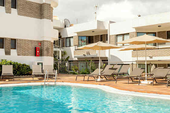 Ulkoallasalue, jossa aurinkotuoleja ja aurinkovarjoja rakennuksen vieressä. (Tekoälyn luoma teksti)