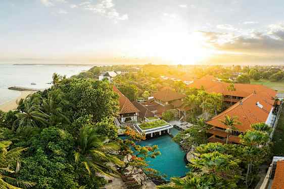 Ulkokuva trooppisesta hotellialueesta, jossa on uima-allas ja taustalla meri auringonnousun aikaan. (Tekoälyn luoma teksti)