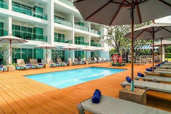 Uima-allasalue aurinkotuoleineen, varjoineen ja moderni rakennus taustalla. (Tekoälyn luoma teksti)