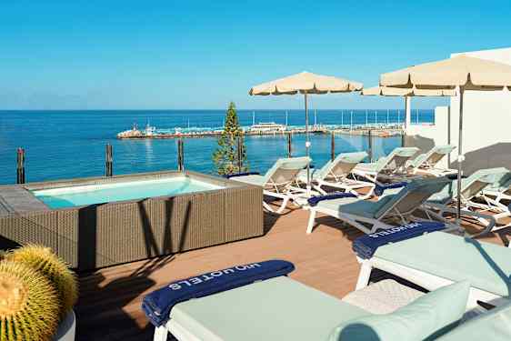 Terassi aurinkotuoleilla ja aurinkovarjoilla porealtaan vieressä, josta on merinäköala. (Tekoälyn luoma teksti)