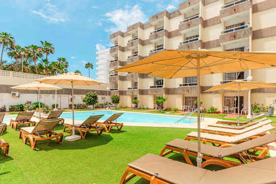 Ulkotila, jossa aurinkotuoleja, aurinkovarjoja ja uima-allas hotellin edessä. (Tekoälyn luoma teksti)