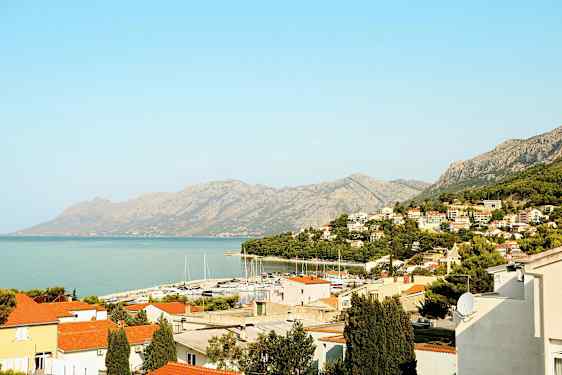 Näkymä rannikkokaupunkiin, jossa on punaisia ​​kattoja, venesatama ja vuoria taustalla. (Tekoälyn luoma teksti)