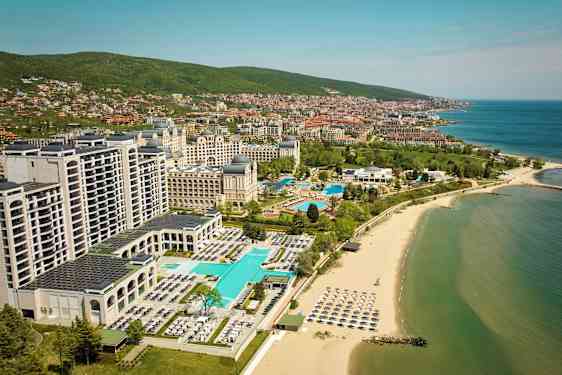 Hotellit ja uima-altaat rannalla, taustalla meri ja kaupunki. (Tekoälyn luoma teksti)