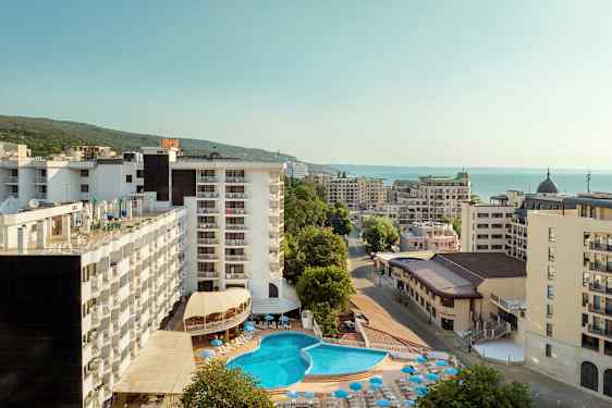 Hotellirakennukset ulkouima-altaalla ja aurinkotuoleilla, ympärillä muita rakennuksia lähellä merta. (Tekoälyn luoma teksti)