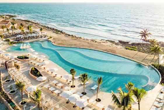 Suuri uima-allas, jota ympäröivät aurinkotuolit ja varjot, sijaitsee rannalla merinäköalalla. (Tekoälyn luoma teksti)