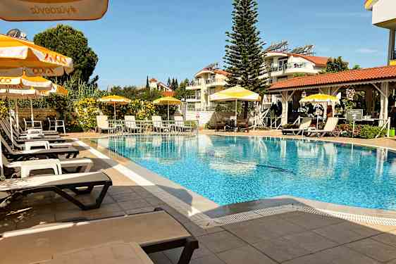 Ulkouima-allas, jossa aurinkotuoleja ja aurinkovarjoja, ympärillä vehreyttä ja rakennuksia. (Tekoälyn luoma teksti)