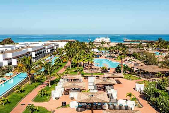 Lomakeskus valkoisilla rakennuksilla, uima-allas ja ympäröivä vihreä alue, taustalla meri. (Tekoälyn luoma teksti)