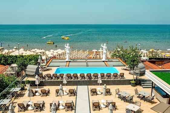 Näkymä altaalle, jossa on aurinkotuoleja, patsaita ja hiekkaranta meren äärellä. (Tekoälyn luoma teksti)