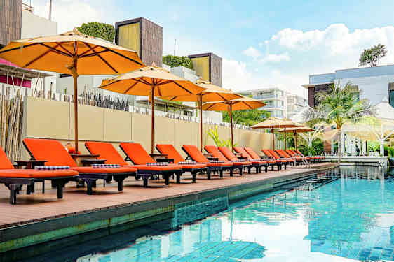 Ulkouima-allas, jonka reunalla on oransseja aurinkotuoleja ja varjoja, ympäröity modernilla arkkitehtuurilla. (Tekoälyn luoma teksti)