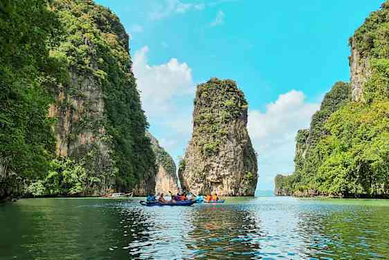 Useat henkilöt melovat kajakkeja kauniin maiseman läpi, korkeiden vihreiden kallioiden välissä. (Tekoälyn luoma teksti)