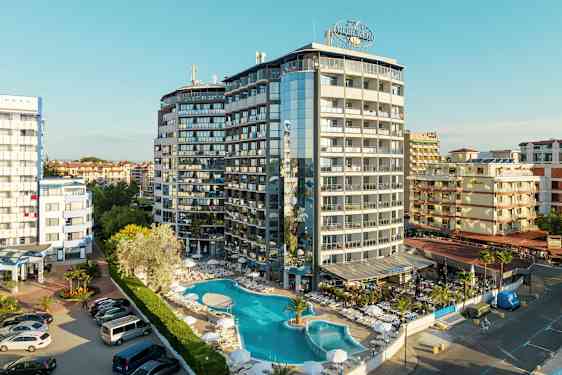 Monikerroksinen hotelli, jonka edessä on uima-allas ja aurinkotuoleja, sijaitsee tiheään rakennetulla alueella. (Tekoälyn luoma teksti)