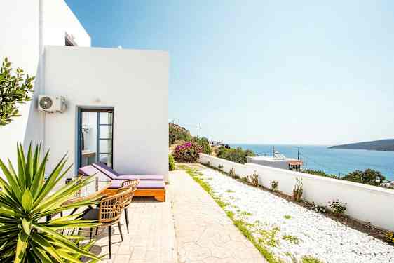 Valkoinen rakennus aurinkotuoleilla ja pöydällä terassilla, joka avautuu merelle. (Tekoälyn luoma teksti)