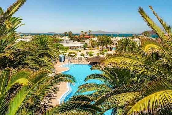 Näkymä uima-altaalle, jonka ympärillä on palmupuita, ja kaukana näkyy meri. (Tekoälyn luoma teksti)