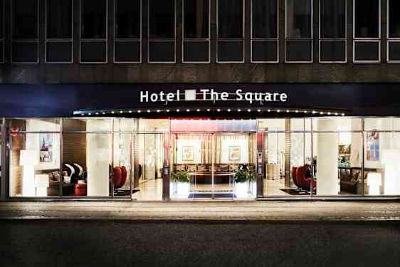 Hotel The Squaren julkisivu ja pääsisäänkäynti, jossa on lasiovet ja suuret ikkunat. (Tekoälyn luoma teksti)