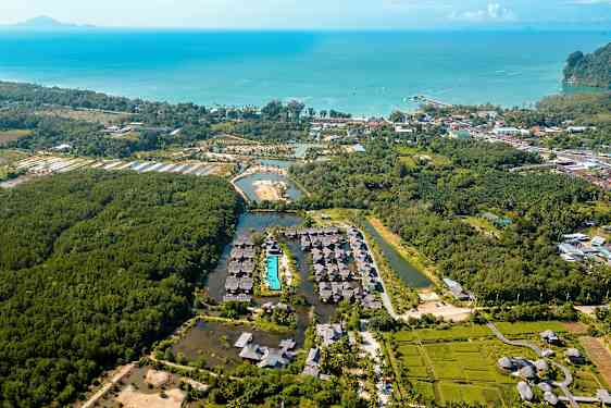 Ilmakuva lomakeskuksesta, jota ympäröi kasvillisuus; keskiössä uima-allas ja taustalla meri. (Tekoälyn luoma teksti)