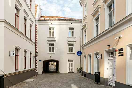 Kapea katu, jota ympäröivät vaaleat rakennukset ikkunoineen ja ovineen. (Tekoälyn luoma teksti)