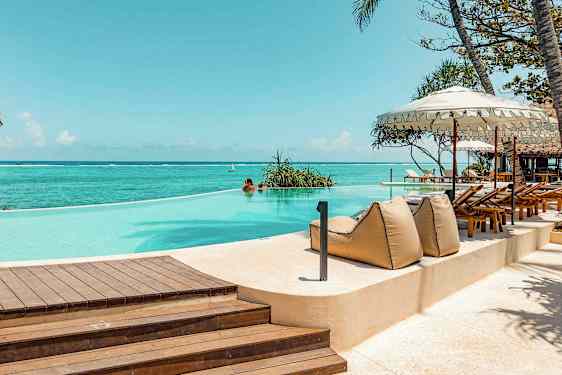 Infiniteettiuima-allas meren äärellä, ympäröity aurinkotuoleilla ja varjoilla. (Tekoälyn luoma teksti)