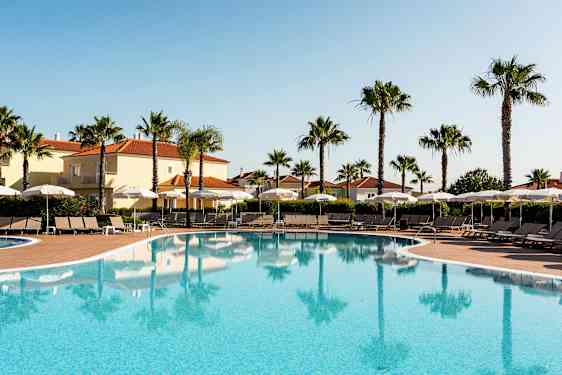 Ulkouima-allas aurinkotuoleilla ja varjoilla, ympärillä palmuja ja rakennuksia, joissa on tiilikatto. (Tekoälyn luoma teksti)