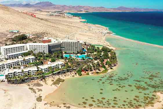 Hotellikompleksi rannalla, jossa turkoosia vettä ja ympärillä autiomaamaisemaa. (Tekoälyn luoma teksti)