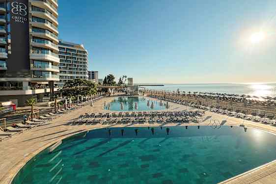 Hotellirakennus rantakadulla, uima-allas ja aurinkotuolit. (Tekoälyn luoma teksti)