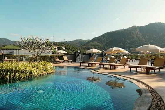 Ulkouima-allas aurinkotuoleineen ja päivänvarjoineen, ympärillä vihreää kasvillisuutta ja taustalla vuoria. (Tekoälyn luoma teksti)