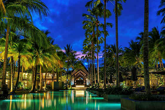 Iltaisin kuva valaistusta uima-altaasta ja korkeista palmuista lomakohteessa. (Tekoälyn luoma teksti)