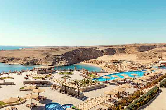 Näkymä rannalle, jossa on aurinkovarjoja ja aurinkotuoleja, sekä uima-allas meren vieressä. (Tekoälyn luoma teksti)