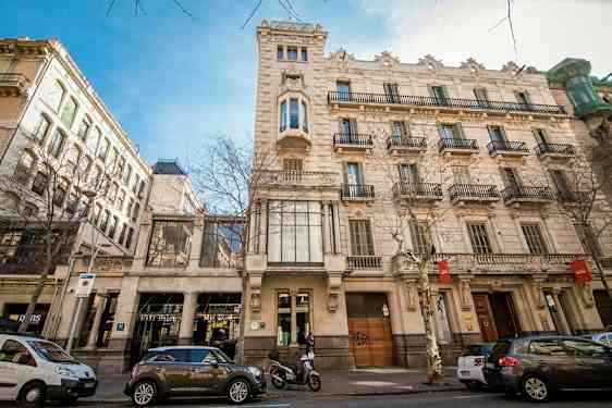 Katu, jonka varrella on klassisia rakennuksia ja pysäköityjä autoja. Julkisivua koristavat ikkunat ja parvekkeet. (Tekoälyn luoma teksti)