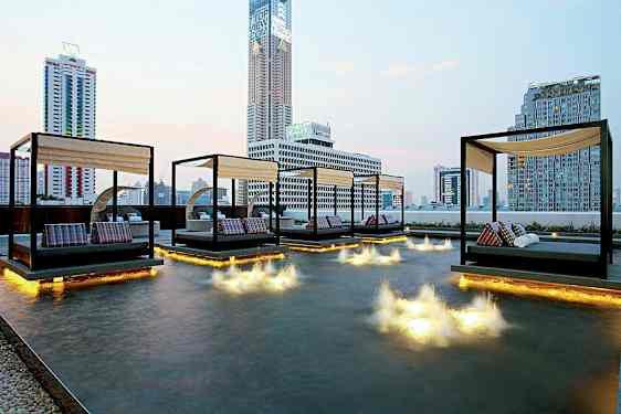 Kuva modernista kaupunkinäkymästä, jossa päivävuoteita sijaitsee matalan altaan yläpuolella, jossa on valoinstallaatioita vedessä. (Tekoälyn luoma teksti)