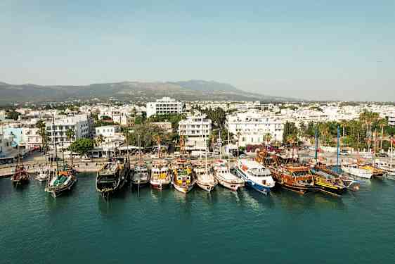 Satama, jossa useita veneitä kiinnitettynä, ja kaupunki valkoisine rakennuksineen taustalla. (Tekoälyn luoma teksti)