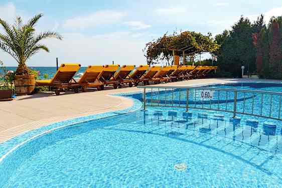 Uima-allas matalalla vedellä keltaisten aurinkotuolien rivin edessä terassilla, taustalla meri. (Tekoälyn luoma teksti)