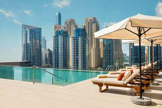 Aurinkotuoleja infinity-altaan äärellä, näkymä kaupunkiin, jossa on korkeita rakennuksia. (Tekoälyn luoma teksti)