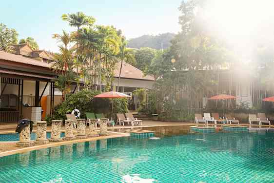 Ulkouima-allas, jolla on aurinkotuoleja ja aurinkovarjoja, vehreiden puiden ympäröimänä. (Tekoälyn luoma teksti)