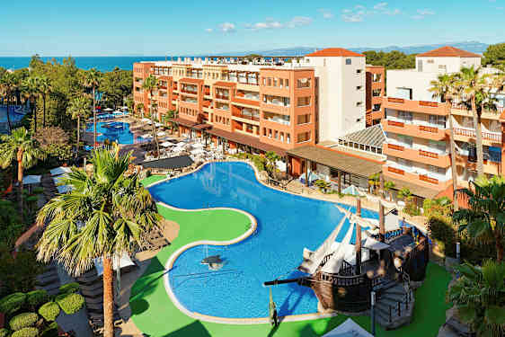 Hotellialue, jossa suuri uima-allas, ympärillä palmuja ja rakennuksia. (Tekoälyn luoma teksti)