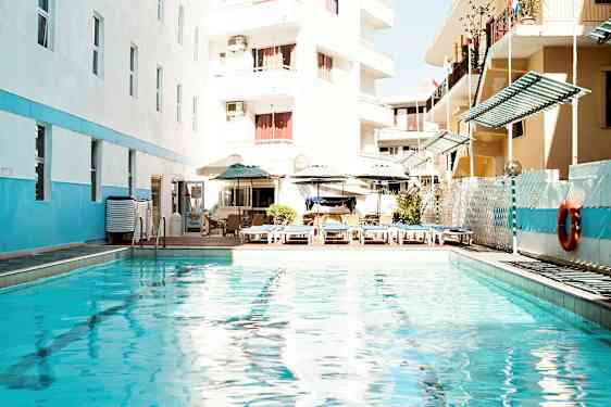 Ulkouima-allas aurinkotuoleilla ja -varjoilla, rakennusten ympäröimä. (Tekoälyn luoma teksti)