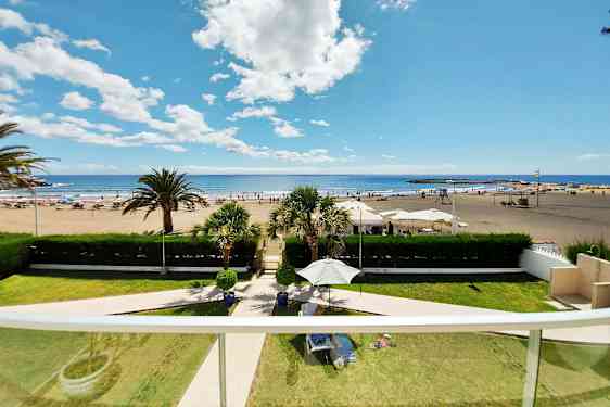 Näkymä parvekkeelta hiekkarannalle, jossa on aurinkotuoleja ja päivänvarjoja, sekä merelle ja taivaalle. (Tekoälyn luoma teksti)